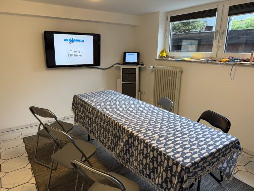 Ein besprechungsraum mit Tisch, Stühlen und zwei Bildschirmen.